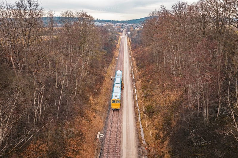 Long view of a rail line with a yellow train through a wintery forest, using a tamping machine at the Hermann Hessebahn construction site, Calw, Germany
