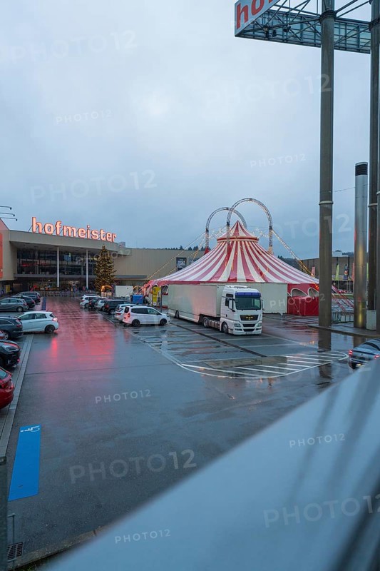 Hofmeister shopping center with circus tent and parked cars at dusk, stuffing machine used at Hermann Hessebahn construction site, Calw, Germany