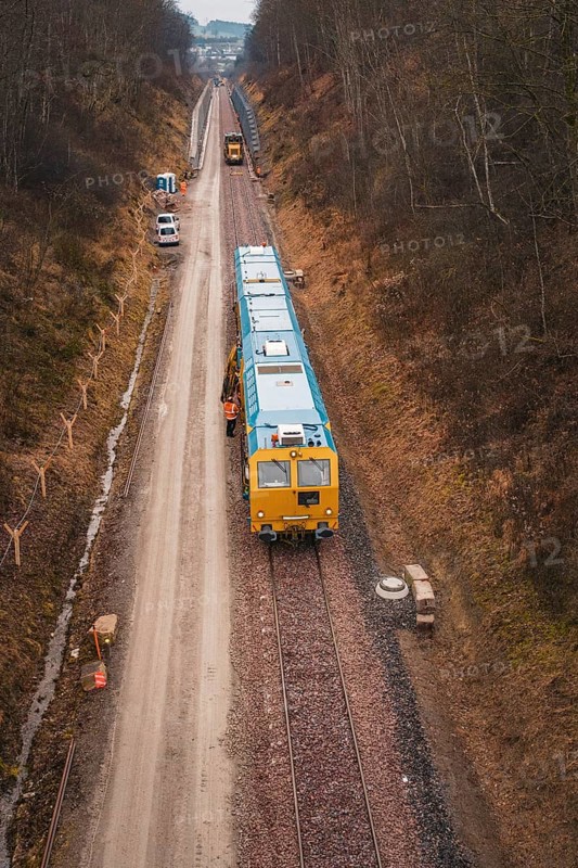 Yellow train on a construction site in a wintry landscape, surrounded by trees, using a tamping machine at the Hermann Hessebahn construction site, Calw, Germany