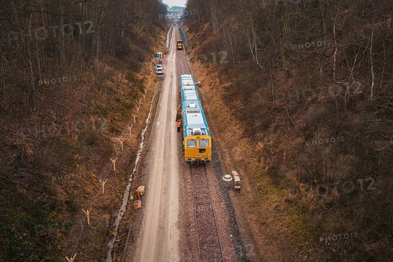 View of a railway line with a yellow train in a lightly wooded area, tamping machine used at the Hermann Hessebahn construction site, Calw, Germany