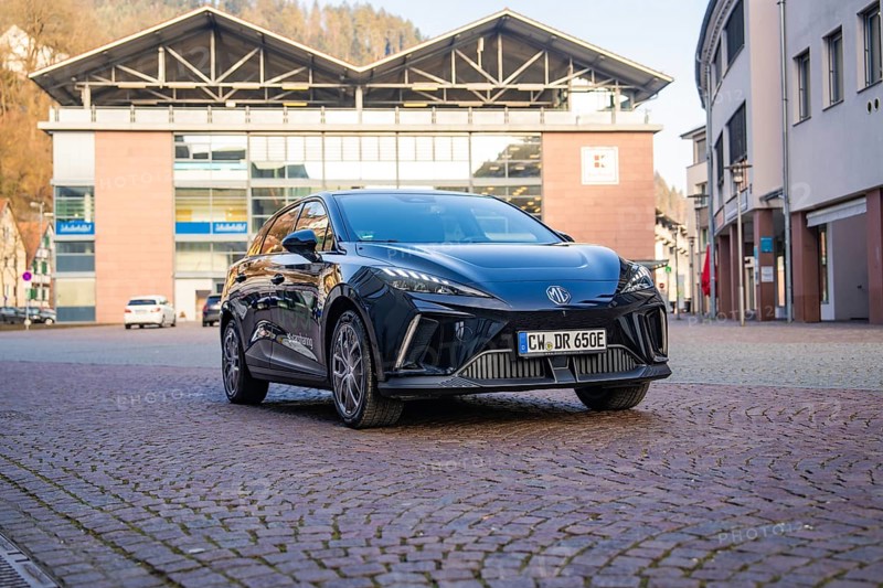 Black car parked in front of modern buildings on a paved area, illuminated by the sun, MG4 electric car, Deer e-Carsharing, Calw, Germany
