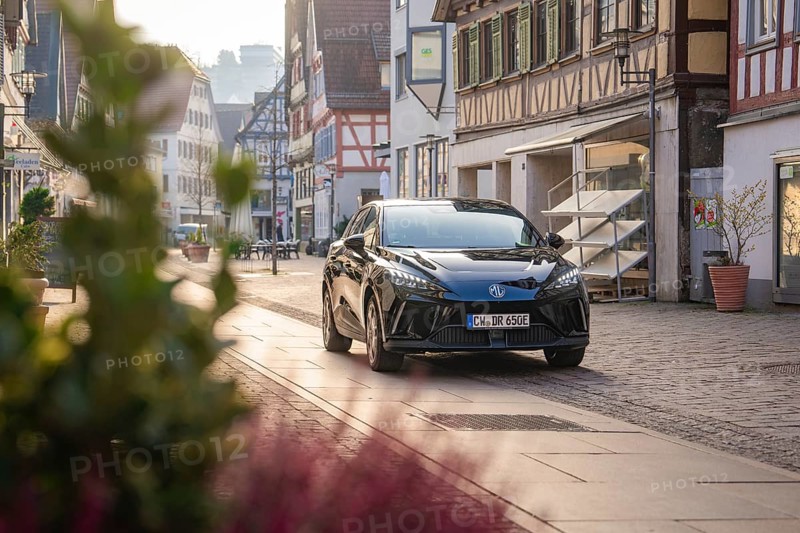 Black car in front of half-timbered houses on a picturesque street with natural light and plants in the foreground, MG4 electric car, Deer e-Carsharing, Calw, Germany