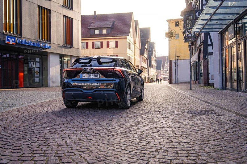 Black car on a paved street in the city with modern and historic architecture in the background at dusk, MG4 electric car, deer e-car sharing, Calw, Germany