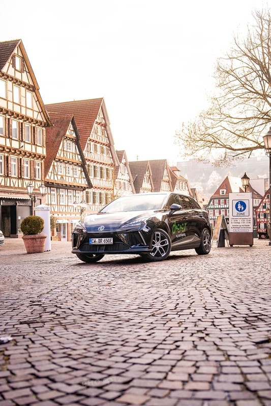 A car is parked in a paved old town and is surrounded by historic buildings and lanterns, MG4 electric car, deer e-car sharing, Calw, Germany