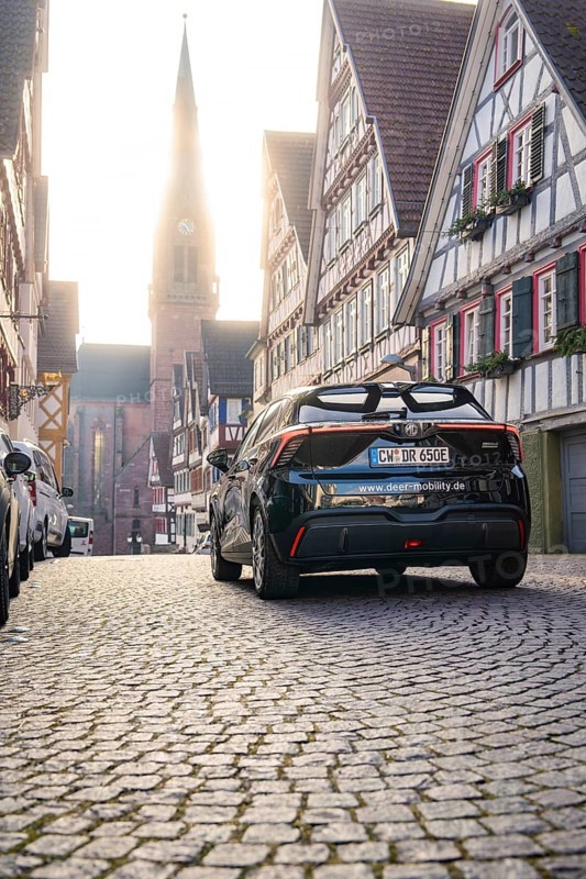Car drives through a picturesque half-timbered road with church in the background at morning light, MG4 electric car, deer e-car sharing, Calw, Germany