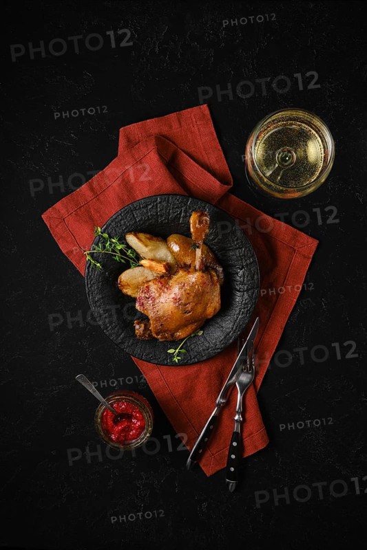 Top view of a plate with roasted duck leg along with caramelised pears and fresh thyme served with a glass of white wine and lingonberry sauce