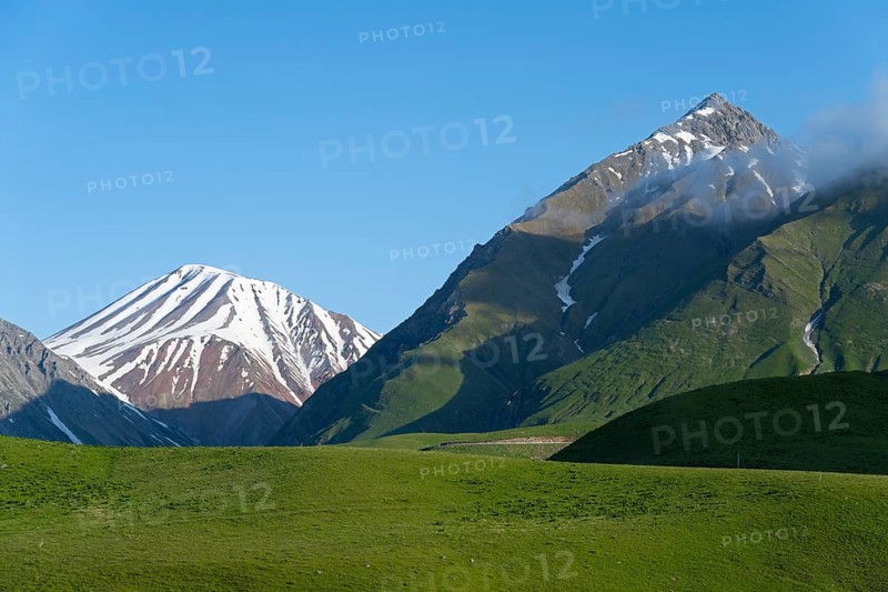 Snow-capped mountains with clouds at the summit, surrounded by green hills, landscape between Kvesheti and Gudauri, Mtskheta-Mtianeti region, Georgian Military Highway, High Caucasus, Georgia