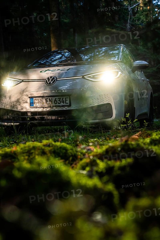 Car with headlights switched on in dark forest on mossy ground, VW ID3 electric car, Deer e-Carsharing, Calw, Germany