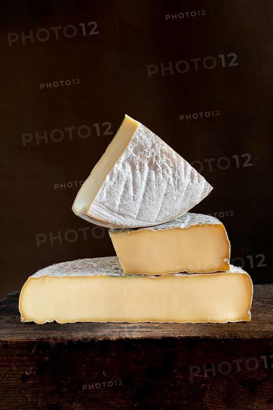 Three pieces of Saint-Nectaire cheese are stacked on top of each other, set on a dark wooden surface, Puy de Dome, Auvergne, France