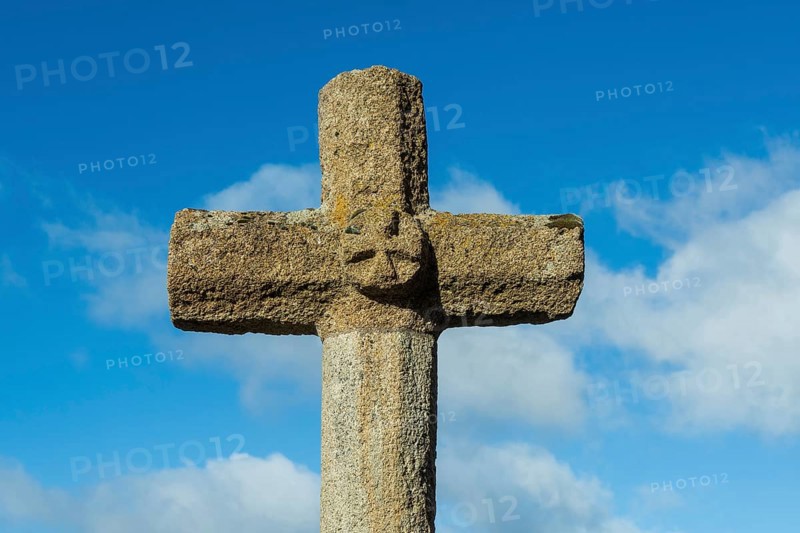 Stone cross stands tall against a bright blue sky with scattered white clouds in the background, creating a religious atmosphere