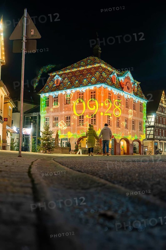 A family looks at a historic building decorated with glowing projections at night, Nagold, Calw district, Black Forest, Germany