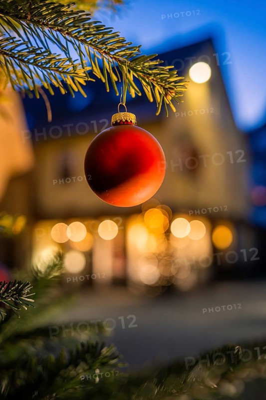 Red Christmas ball on pine branch, evening mood with blurred lights in the background, Nagold, Calw district, Black Forest, Germany