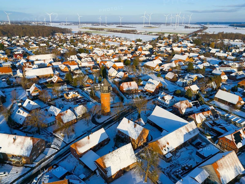 Snowy village with a central water tower surrounded by wind turbines and snow-covered houses under a clear sky, aerial view, water tower, museum, Groß Lafferde, municipality of Ilsede, district of Peine, Lower Saxony, Germany