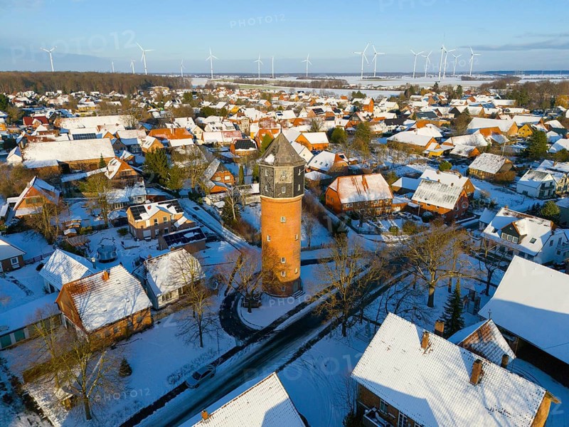 Village with a water tower in the midst of a wintry landscape, surrounded by snow-covered houses and wind turbines, aerial view, water tower, museum, Groß Lafferde, municipality of Ilsede, district of Peine, Lower Saxony, Germany