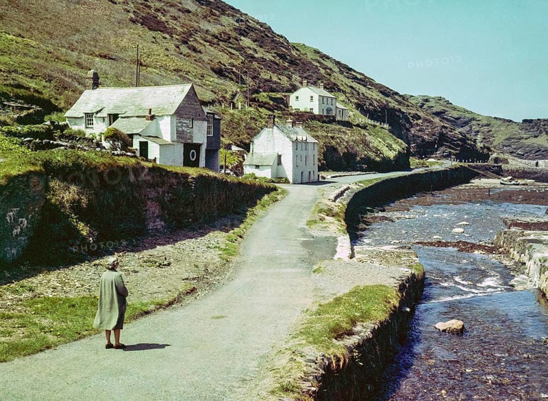 Road passing historic buildings by harbour wall fishing village of Boscastle, Cornwall, England, UK