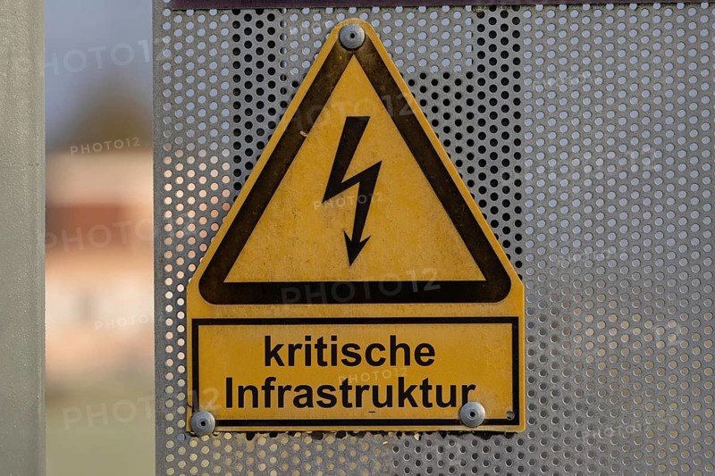 (Photo montage) Text CRITICAL INFRASTRUCTURE on a warning sign for a high-voltage line