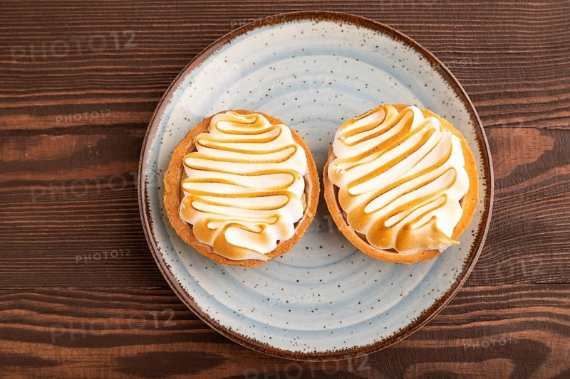French lemon tart with meringue on brown wooden background, top view, flat lay, close up