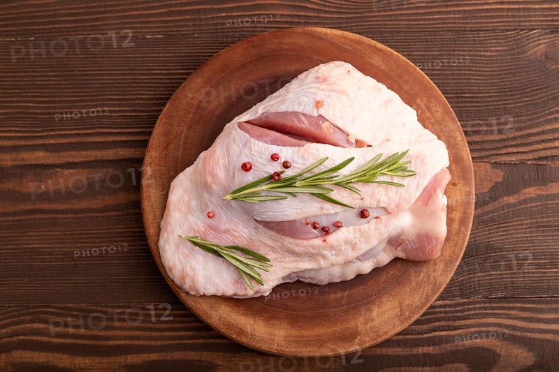 Raw Turkey Thigh with spices and rosemary on cutting board on brown wooden background. top view, flat lay, close up