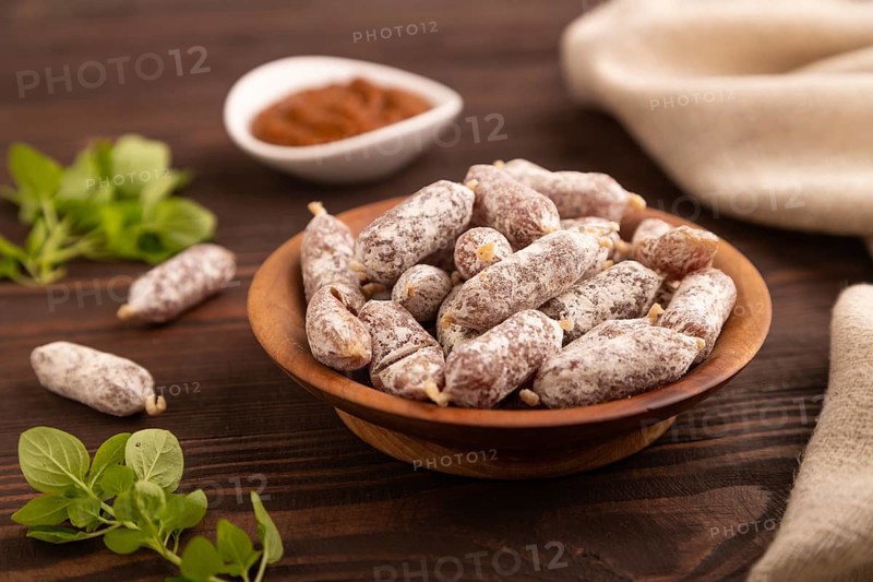 Small smoked Chicken sausages in wooden bowl on brown wooden background and linen textile. side view, close up, selective focus