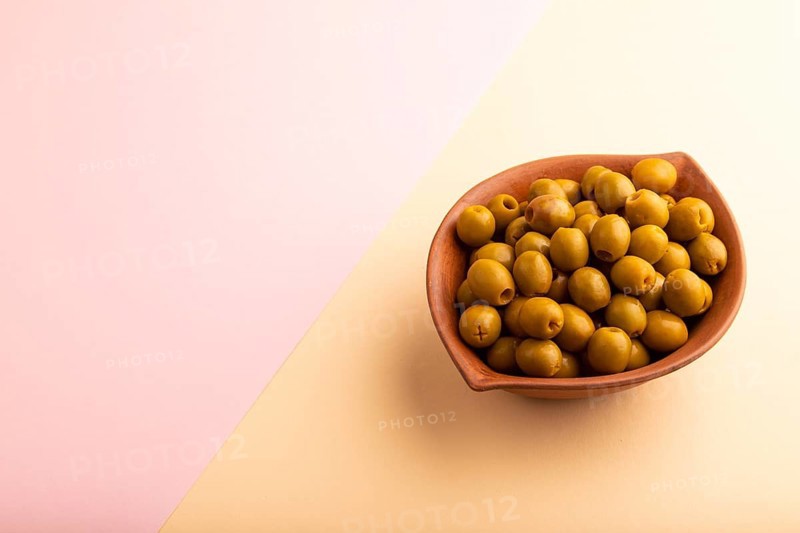 Fresh green olives in ceramic clay bowl on pink and orange pastel paper background. side view, copy space