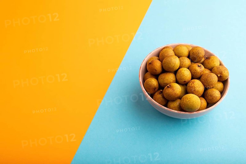 Ripe Longan in ceramic bowl on blue and orange pastel paper background, side view, copy space, minimalism
