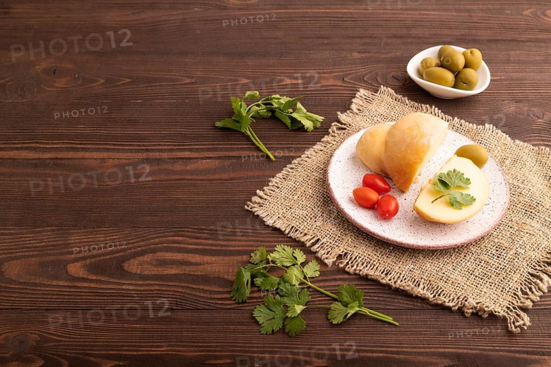 Smoked Mozzarella cheese, with tomatoes and olives on brown wooden background and linen textile, side view, copy space