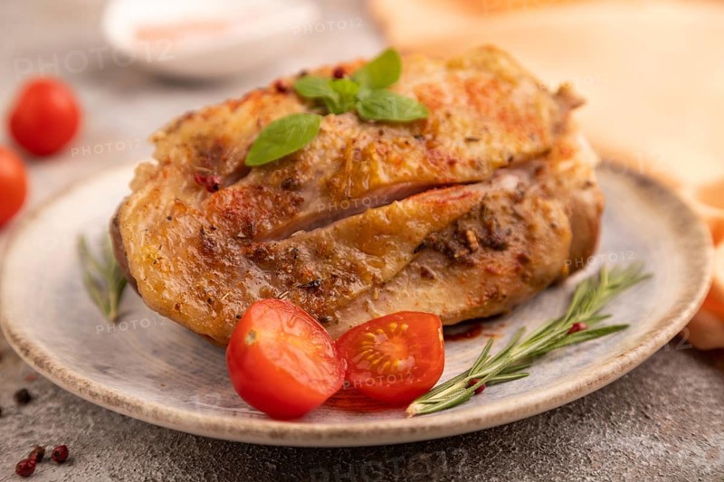 Fried Turkey Thigh with spices and rosemary on plate on brown concrete background and orange linen textile. side view, close up, selective focus