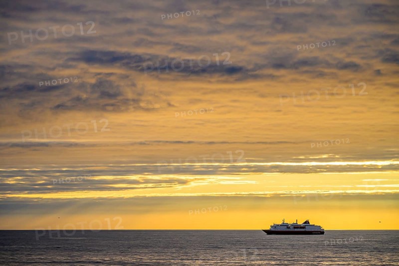 A Hurtigrute ship on the wide Barents Sea at sunset midnight sun, yellowish clouds and calm seas, Berlevåg, Finnmark, Norway