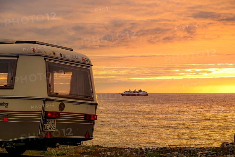 Eriba Touring Troll caravan by the sea, sunset and a Hurtigroute ship on the horizon on the Barents Sea, Berlevåg, Finnmark, Norway