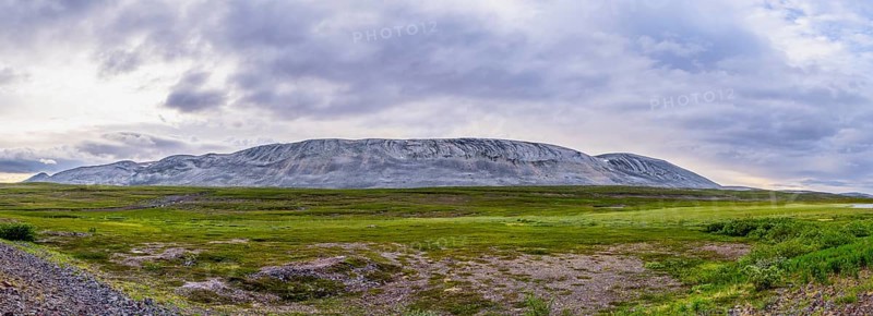 A massive granite rock mountain with bare fells dominates the landscape of the central Varanger Peninsula at Austertanaveien 890 in the foreground, green low fells vegetation wide, quiet landscape, Tana, Finnmark, Norway