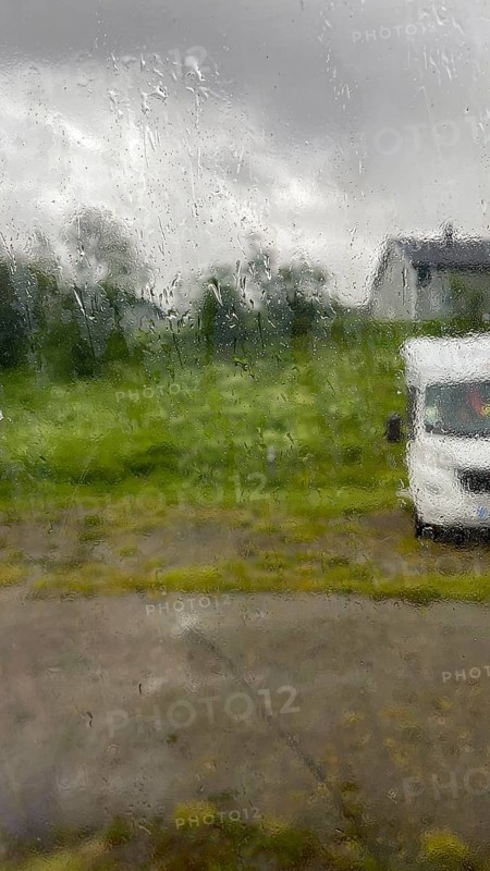 Looking through the rainy glass of a window, rain dripping along the window, cloudy sky, motorhome and green grass, Finnmark, Norway