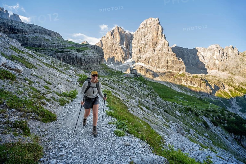 Female mountaineer in front of picturesque mountain landscape in the morning, Rifugio Ai Brentei mountain hut and Cima Tosa rock peak, Brenta, Trentino, Italy