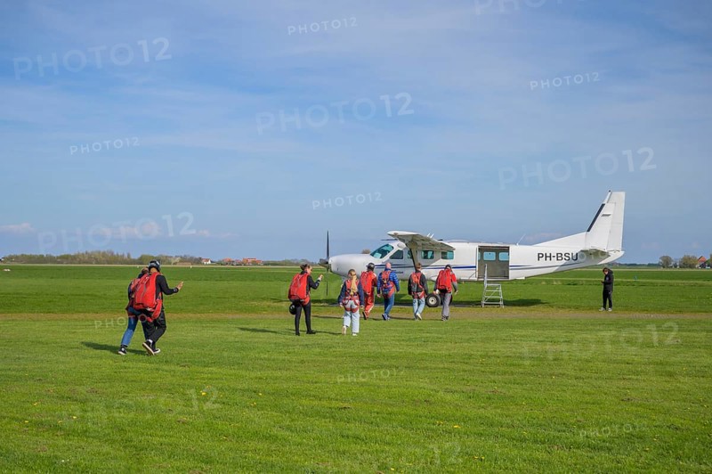 People with parachute equipment in front of a small plane on a green field, taking off for a tandem jump at Paracentrum Texel, North Holland, the Netherlands