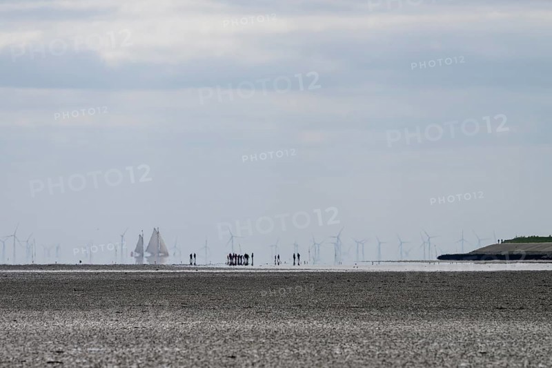 People and sailing ships in the Wadden Sea at low tide with wind turbines on the horizon, people on the beach with boats and wind turbines in the distance, Oosterend, Noord-Holland, the Netherlands