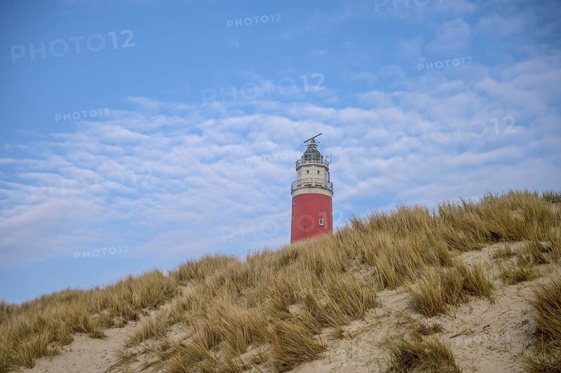 The red lighthouse of De Cocksdorp in the north of the island of Texel rises behind sandy dunes under a blue sky, the Cockdorp, island of Texel, North Holland, the Netherlands