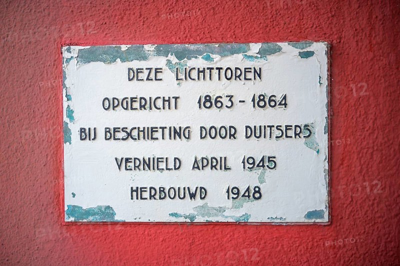 Memorial plaque on a red wall with text about the lighthouse de Cocksdorp and historical events of construction and destruction, Texel island, North Holland, the Netherlands