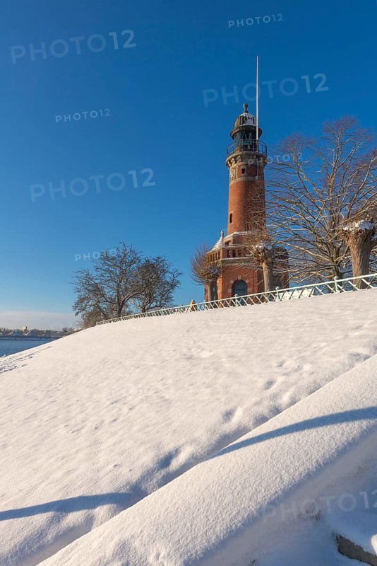 Holtenau lighthouse at the entrance of the Kiel Canal in winter, west bank of the Kiel Fjord, shipping, brick building from 1895, round tower, orientation, sea sign, beacon, ground floor with wedding room, trees, hills, snow, blue sky, Baltic Sea, Kiel, Germany