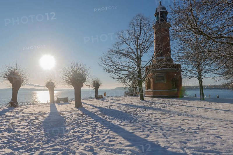 Holtenau lighthouse at the entrance of the Kiel Canal in winter, west bank of the Kiel Fjord, shipping, brick building from 1895, round tower, orientation, sea sign, beacon, ground floor with wedding room, trees, snow, blue sky, back light, sun, Baltic Sea, Kiel, Germany