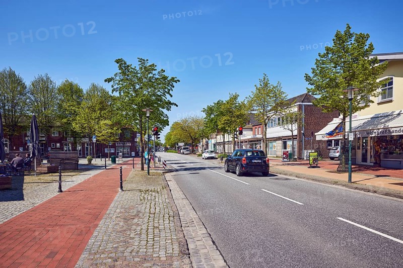 Residential and commercial buildings, general architecture, shops, retail, shopping, sidewalk, bricks, paving stones, street, central strip, vehicles, trees with spring leaves, blue sky, cloudless, main street, barrier bollard, leak, district of North Frisia, Schleswig-Holstein, Germany