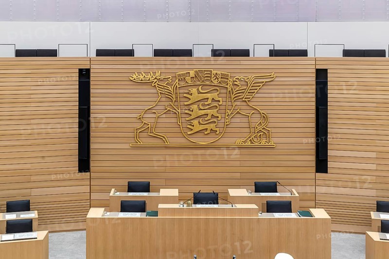 Plenary hall deserted with the seats of deputies and the government bank. Behind it is the coat of arms of the federal state. The state parliament of Baden-Württemberg is the state parliament based in Stuttgart, Baden-Württemberg, Germany