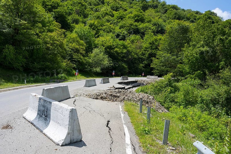 A damaged road with concrete barriers surrounded by dense green forest, road near Naduknari, Kakheti region, Georgia