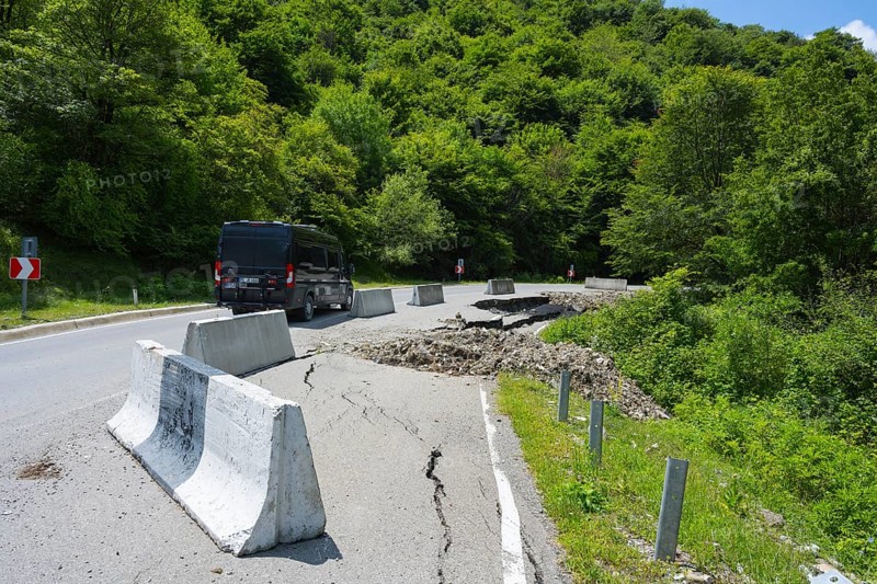 A black van drives on a damaged mountain road with concrete barriers, camper drives on road near Naduknari, Kakheti region, Georgia