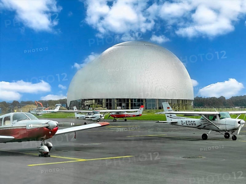 View of flight apron of Essen Mülheim airport with small aircraft parked at the front in the middle of the picture large Zeppelin Hall, Mülheim an der Ruhr, North Rhine-Westphalia, Germany