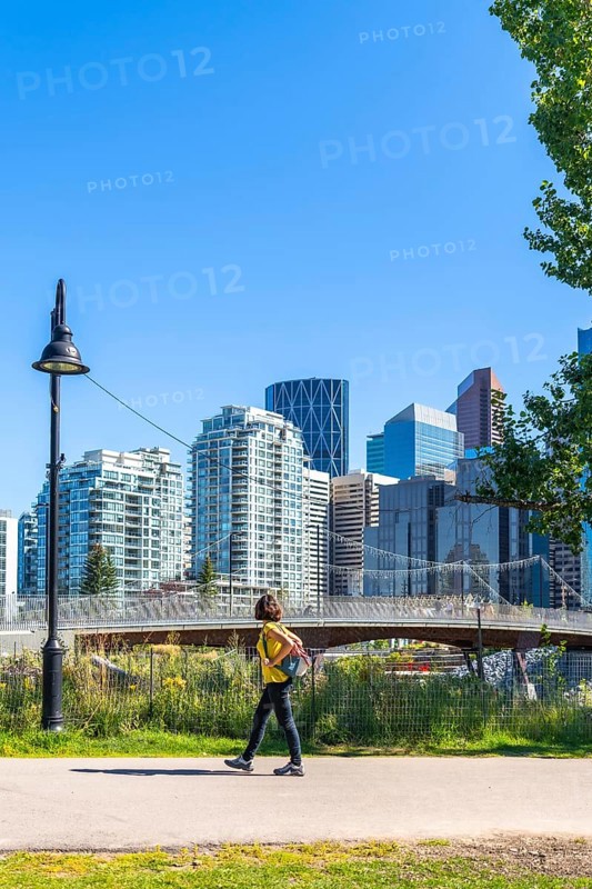 Young woman tourist walking in a city park in calgary, canada, enjoying the summer weather and urban scenery with modern skyscrapers and a pedestrian bridge