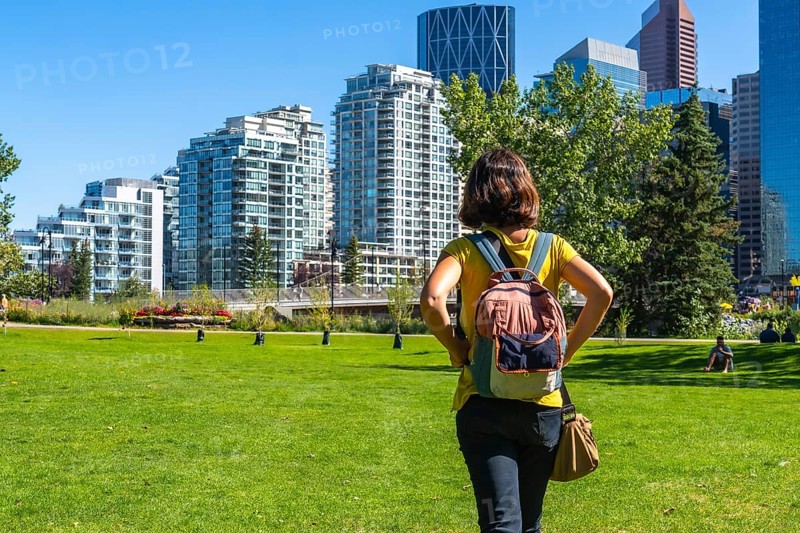 Female tourist with a backpack enjoying a sunny day in calgary's park, taking in the stunning views of the modern skyline and vibrant urban landscape surrounding her