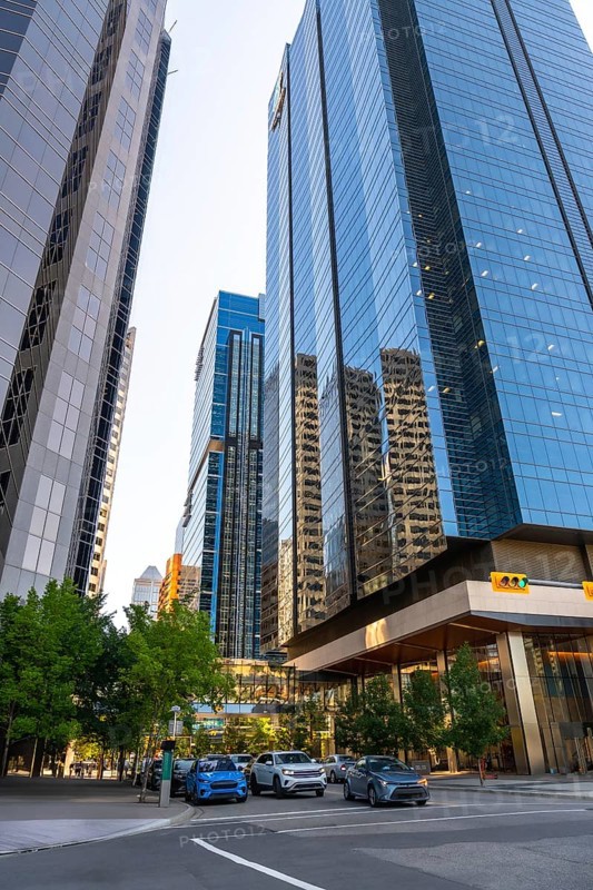 Glass skyscrapers reflecting surrounding buildings rise high above a street with cars passing by in calgary, alberta, canada, creating a dynamic urban scene during the day