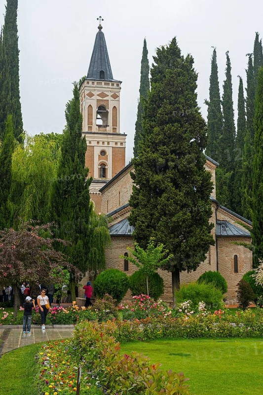 A tall church tower surrounded by blooming gardens and tall trees on a cloudy day, Bodbe monastery, Sighnaghi, Signagi, Kakheti province, Greater Caucasus, Georgia, Western Asia