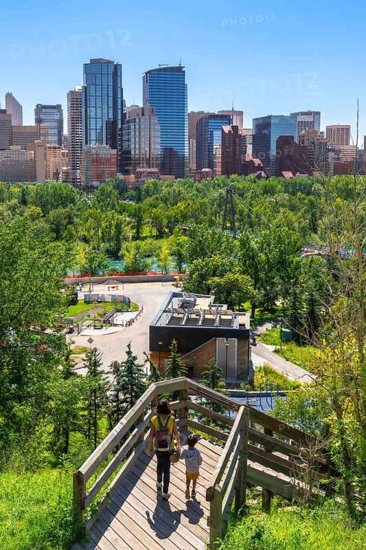 Mother and son descending wooden stairs, enjoying the vibrant urban park with the stunning calgary skyline in the background on a bright, sunny summer day