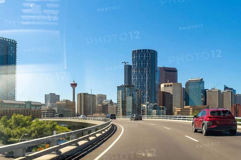 Cars driving along a highway showcase the vibrant calgary skyline, featuring the iconic calgary tower, under a bright blue sky on a sunny summer day
