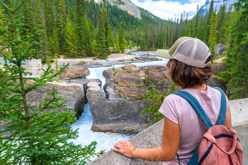 Female tourist wearing a baseball cap and backpack, admiring the bow river natural bridge in banff national park, alberta, a stunning landmark shaped by erosion